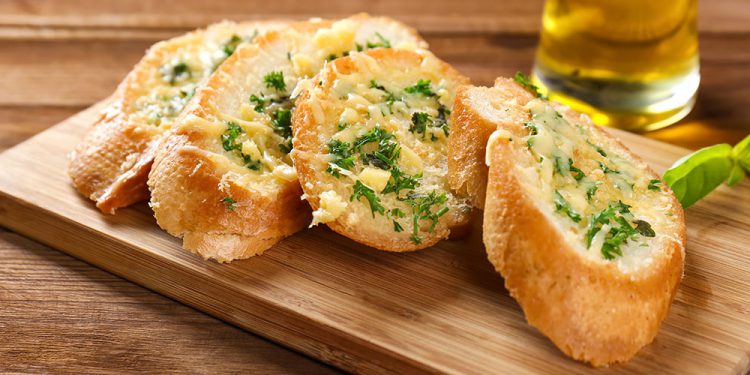 Pão de Alho em uma tabua de madeira. Petiscos são ótimos para fazer um churrasco barato.